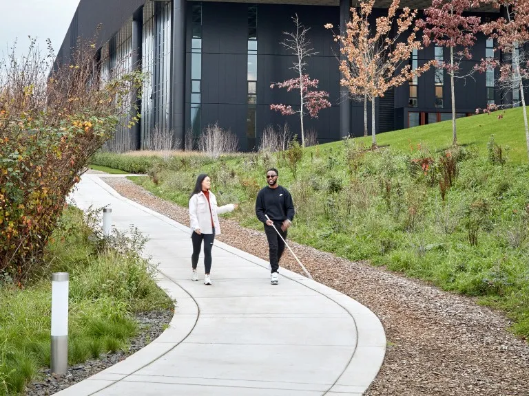Two people walking on a curved path next to a modern building and autumn trees