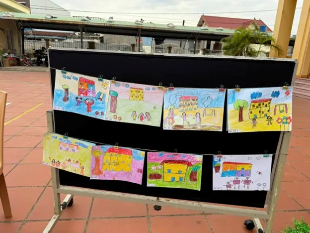 Bé hoàn thiện các chi tiết cuối cùng cho bức tranh vẽ chủ đề trường mầm non