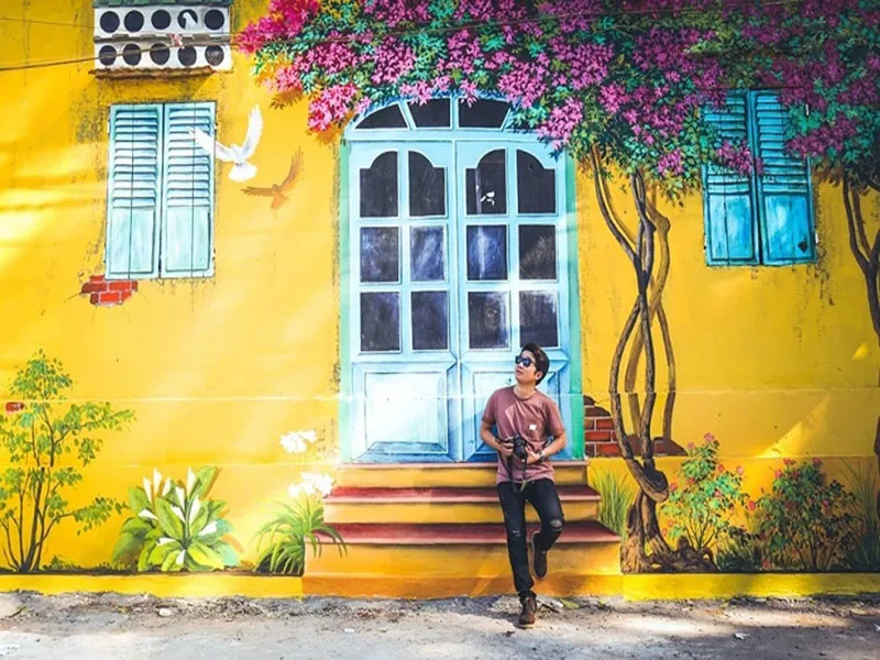 Các bạn trẻ chụp ảnh check-in bên bức tranh tường vẽ hoa giấy rực rỡ trên nền tường vàng